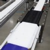 Three different color plastic pallets move between locating stations on a VersaFlex conveyor system.